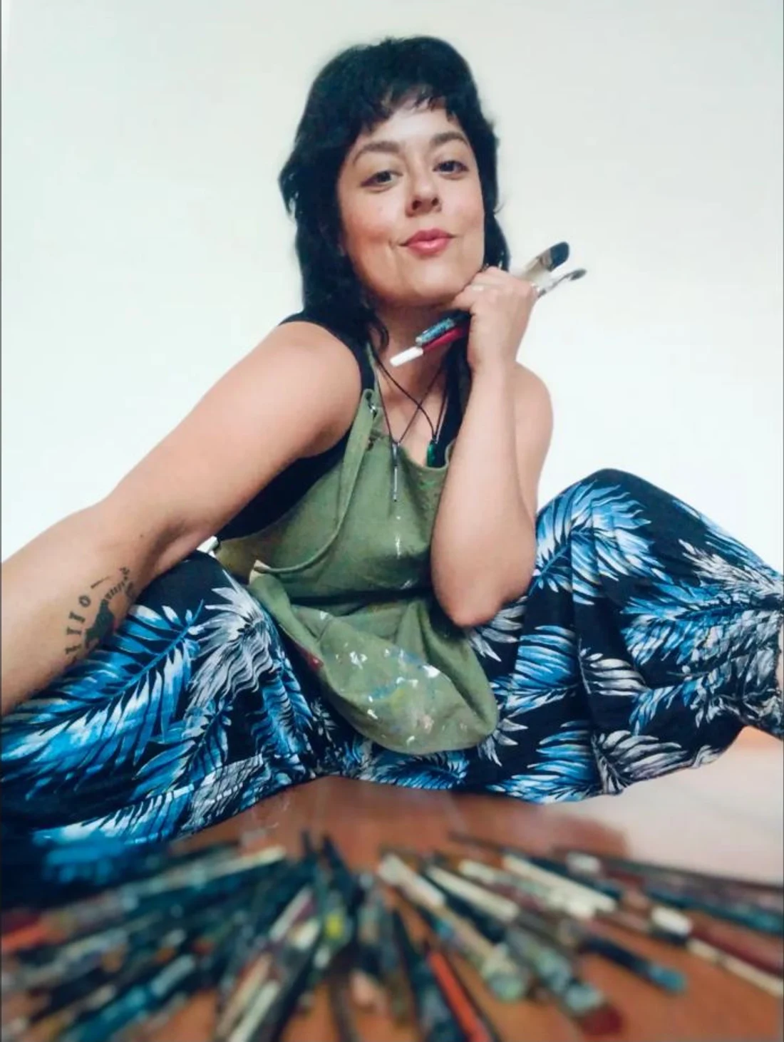 Dayis seated in her paint-covered apron, holding paintbrushes